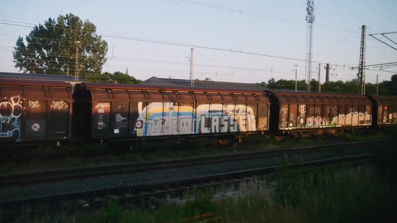 In treno, passando accanto a un vagone e ai binari, con un ampio tramonto.