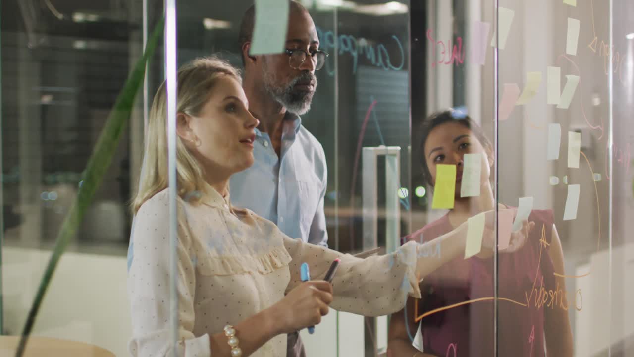 Professional businesspeople discussing together over a glassboard in modern office in slow motion