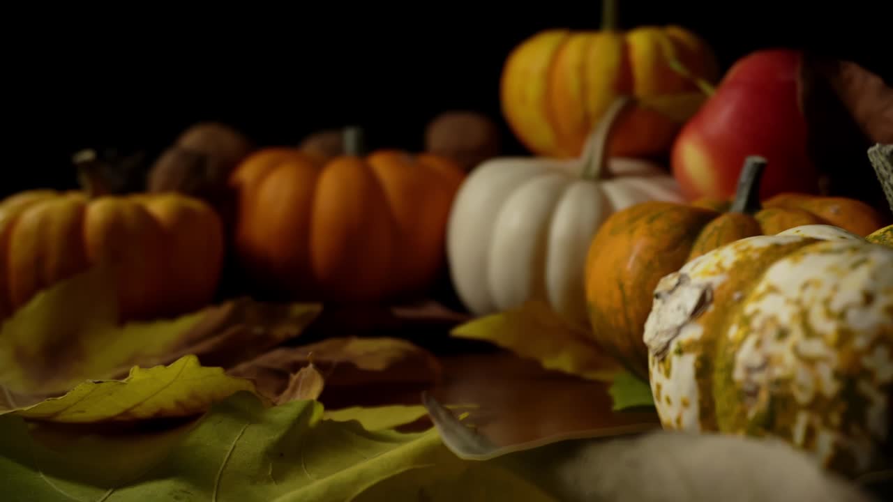 Macro footage with bokeh of autumn still life made of pumpkins and maple leaves on black background