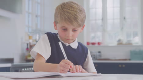 boy at home wearing school uniform doing homework on kitchen counter