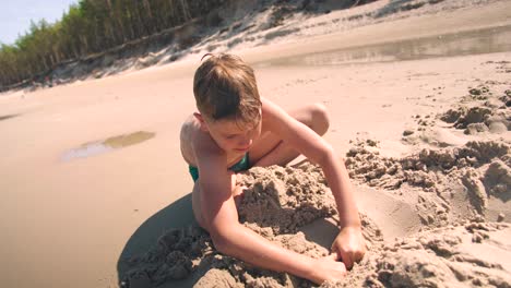 young boy at beach is busy digging a hole in the sand with shovel