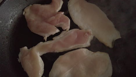 top down, chicken fillets cook in steaming frying pan, closeup detail