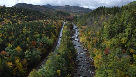 cars driving highway next to river during fall colors, aerial shot