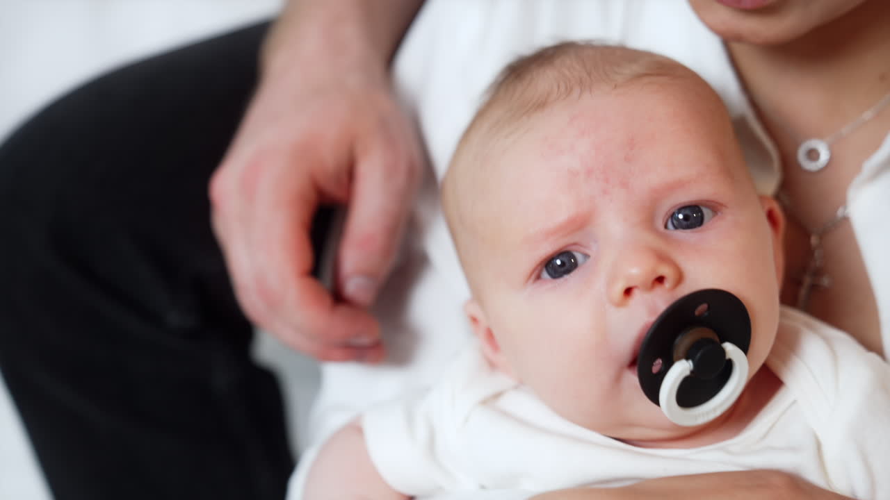 Face of a tiny Caucasian newborn boy with a pacifier in mouth. Baby is dandled in mom's hands.