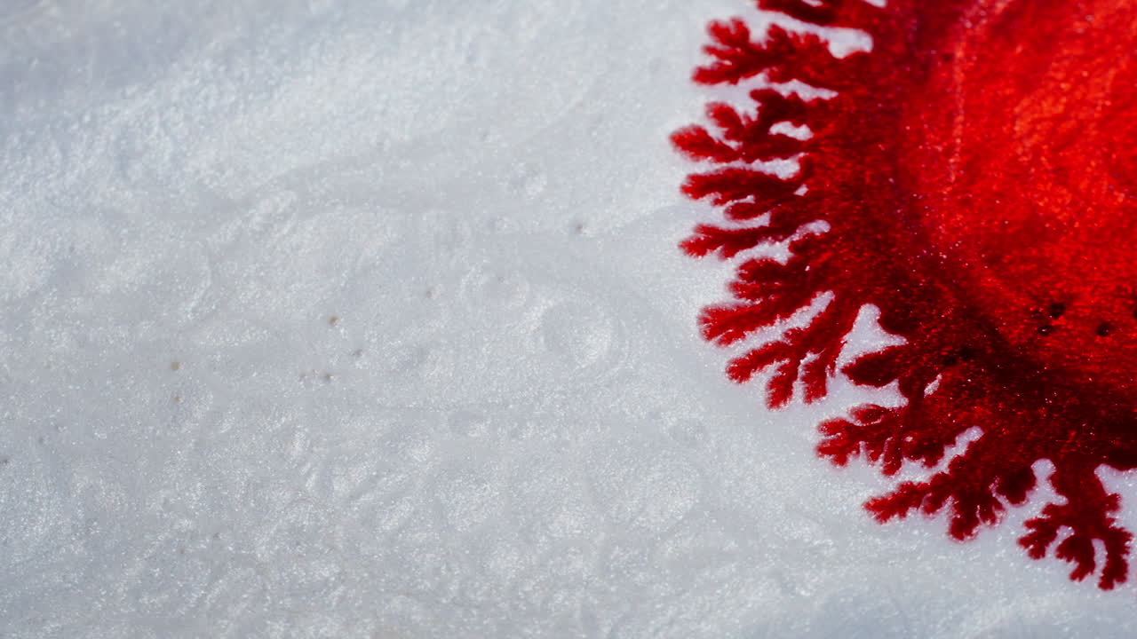 Red ink spreading like poison on a watery white background. Macro view