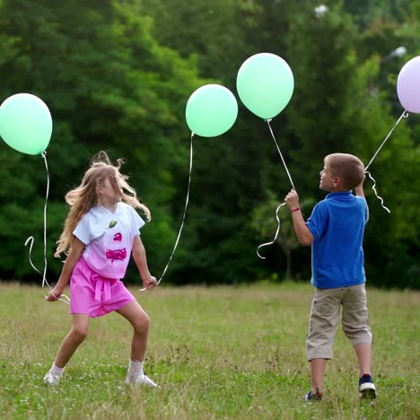 boy and girl are playing with baloons outside. happy children jump on grass in summer. family day on weekend. happiness concept