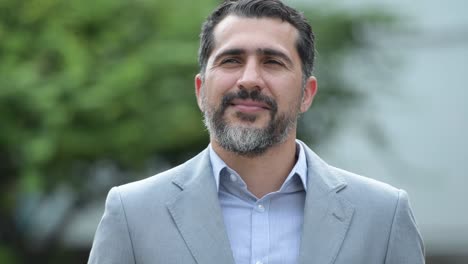 persa guapo hombre de negocios barbudo sonriendo mientras piensa en las calles al aire libre