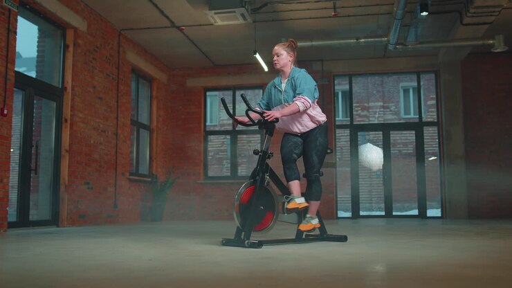 Healthy Caucasian woman exercising workout on stationary cycling machine bike in gym, Slow Motion