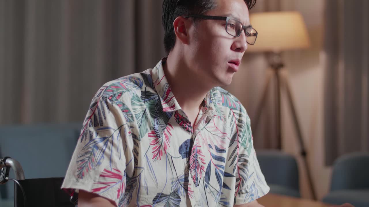 primer plano de un hombre asiático cansado en silla de ruedas sacudiendo la cabeza y teniendo dolor de cabeza mientras edita el video por un escritorio al lado de la cámara en casa