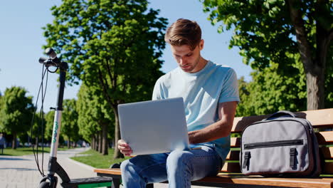 man working on laptop in a park with electric scooter