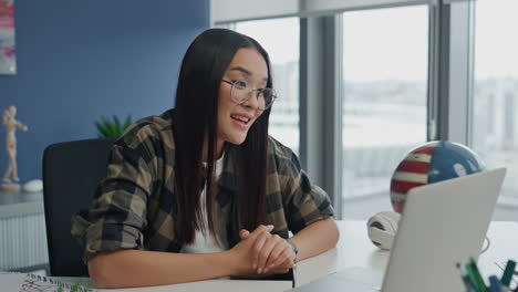 Mujer-Positiva-Saludando-Videollamada-Portátil-En-El-Primer-Plano-De-La-Oficina.-Estudiante-Hablando