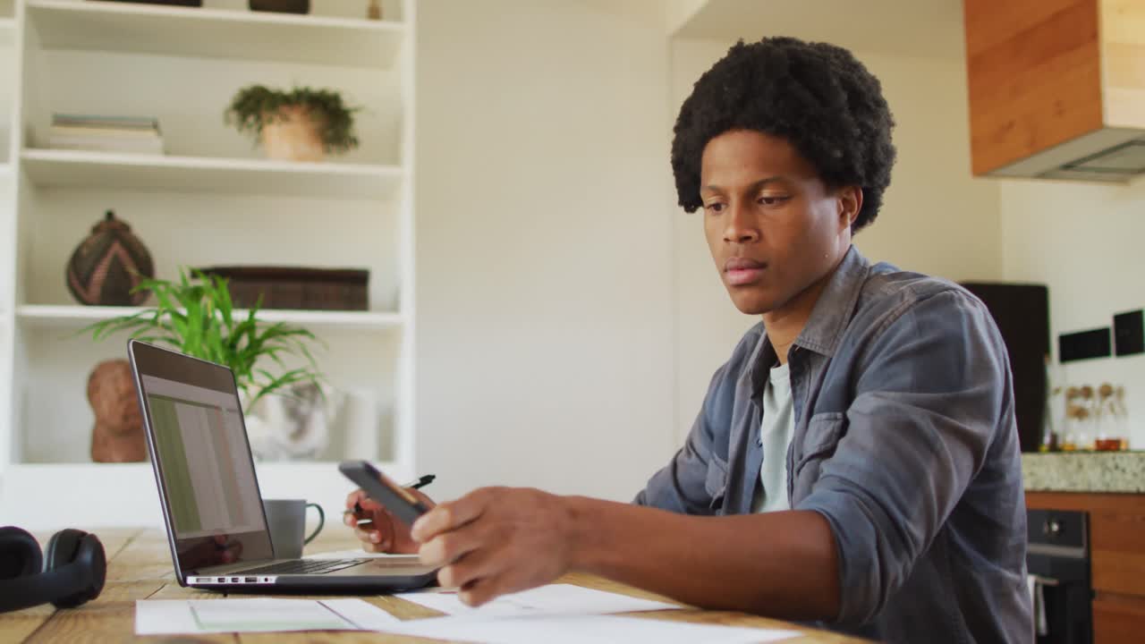 Uomo afroamericano che lavora da casa e usa laptop e smartphone