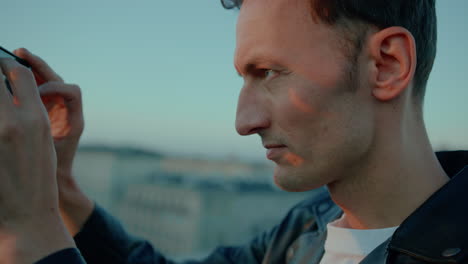 Caucasian man takes pictures with phone from rooftop, side close-up