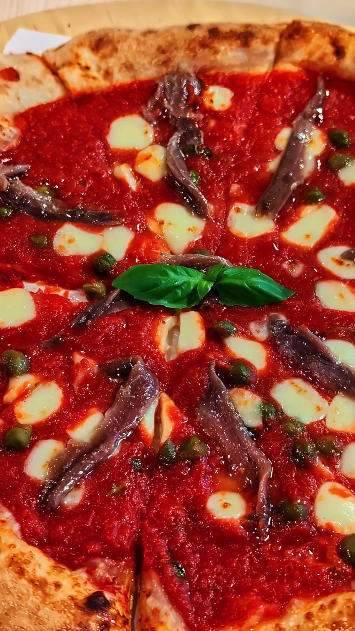 Primo piano di una pizza con acciughe e basilico su un tavolo di legno.