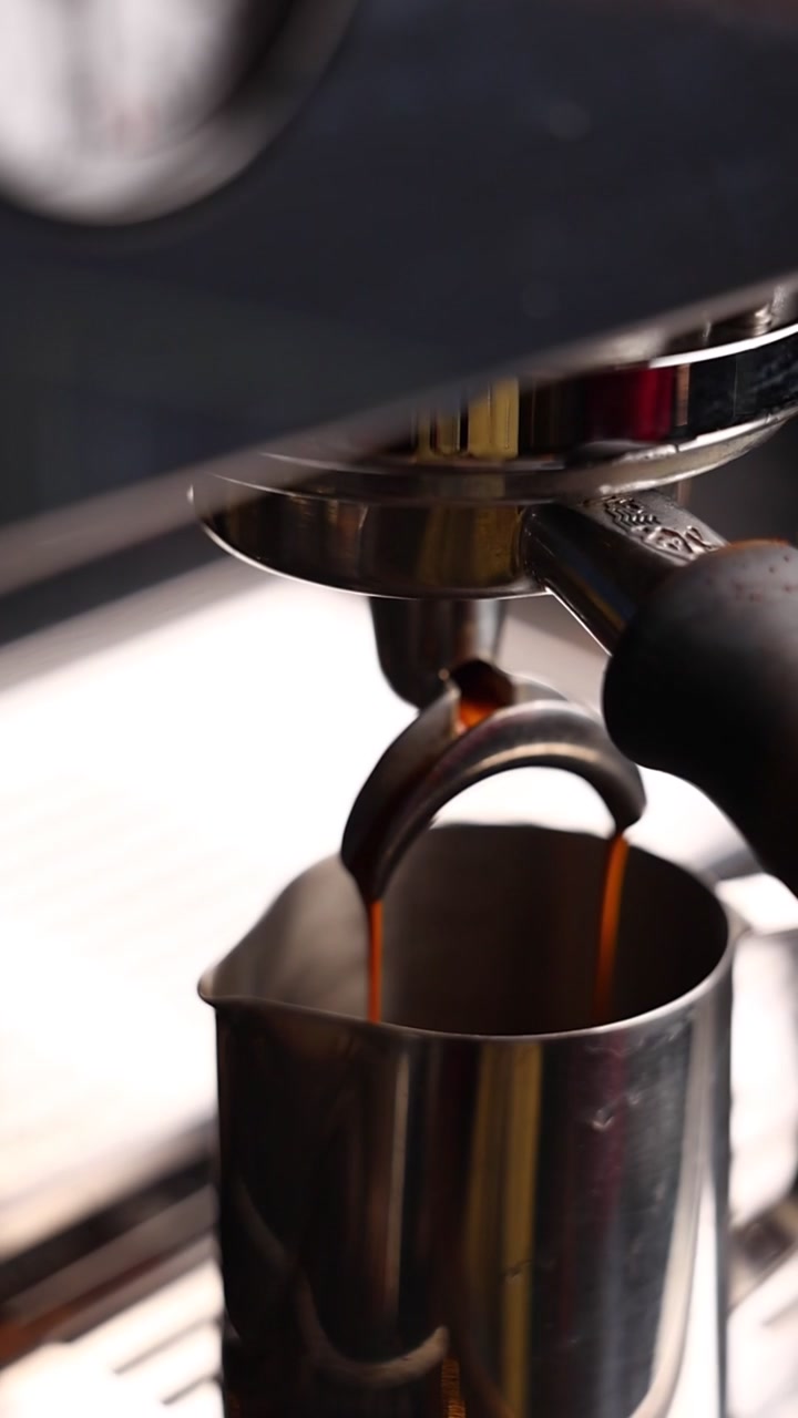 Espresso che cola dal portafiltro in una lattiera di metallo