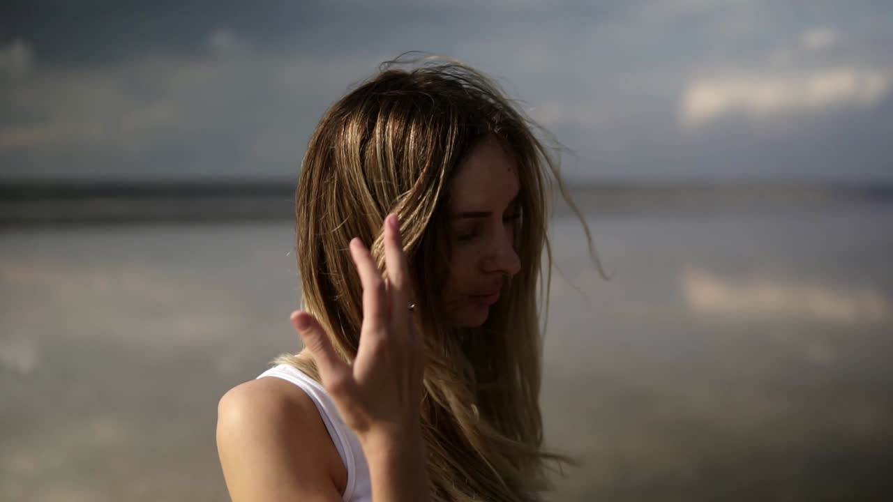 retrato de una mujer de pelo largo de pie frente al lago con el cielo reflejado en el espejo