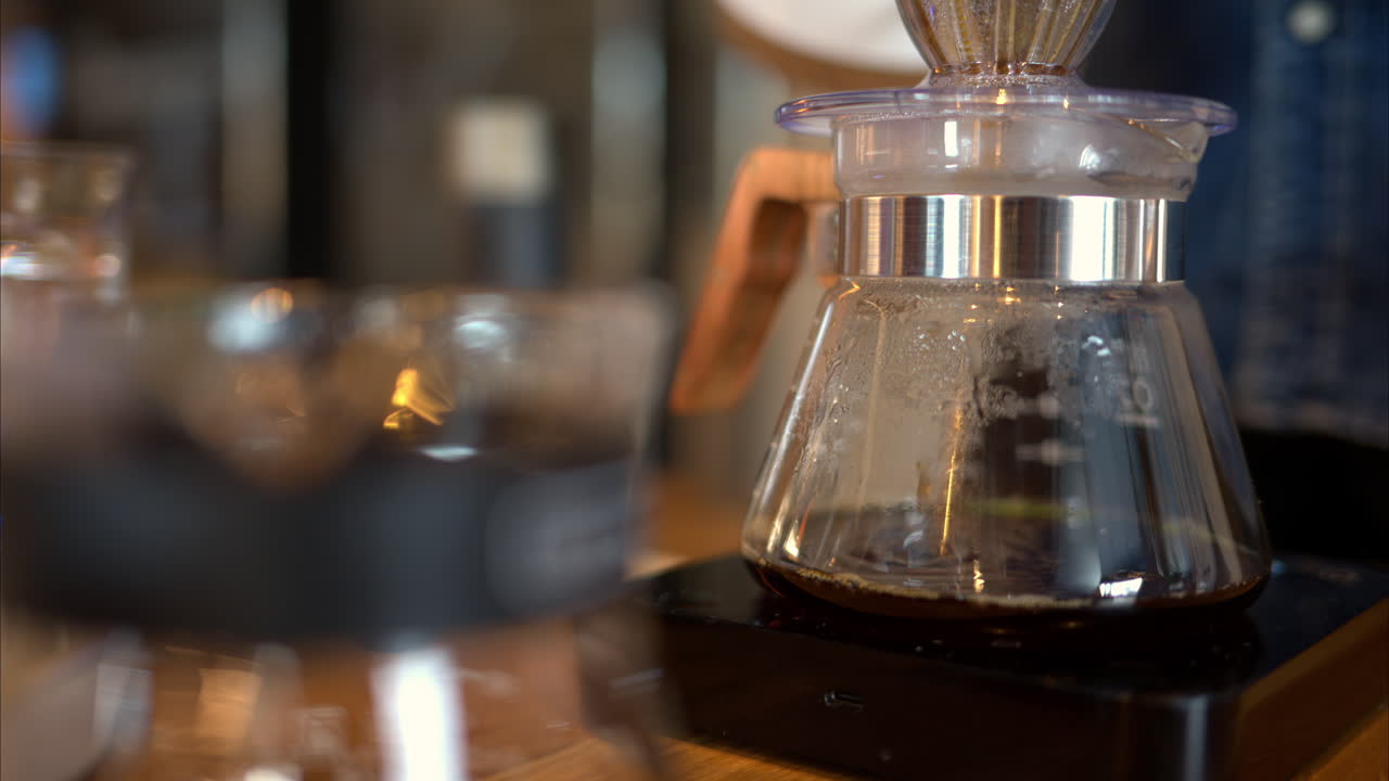 Close up of a man brewing pour-over drip coffee in a slow, circular motion on a wooden table
