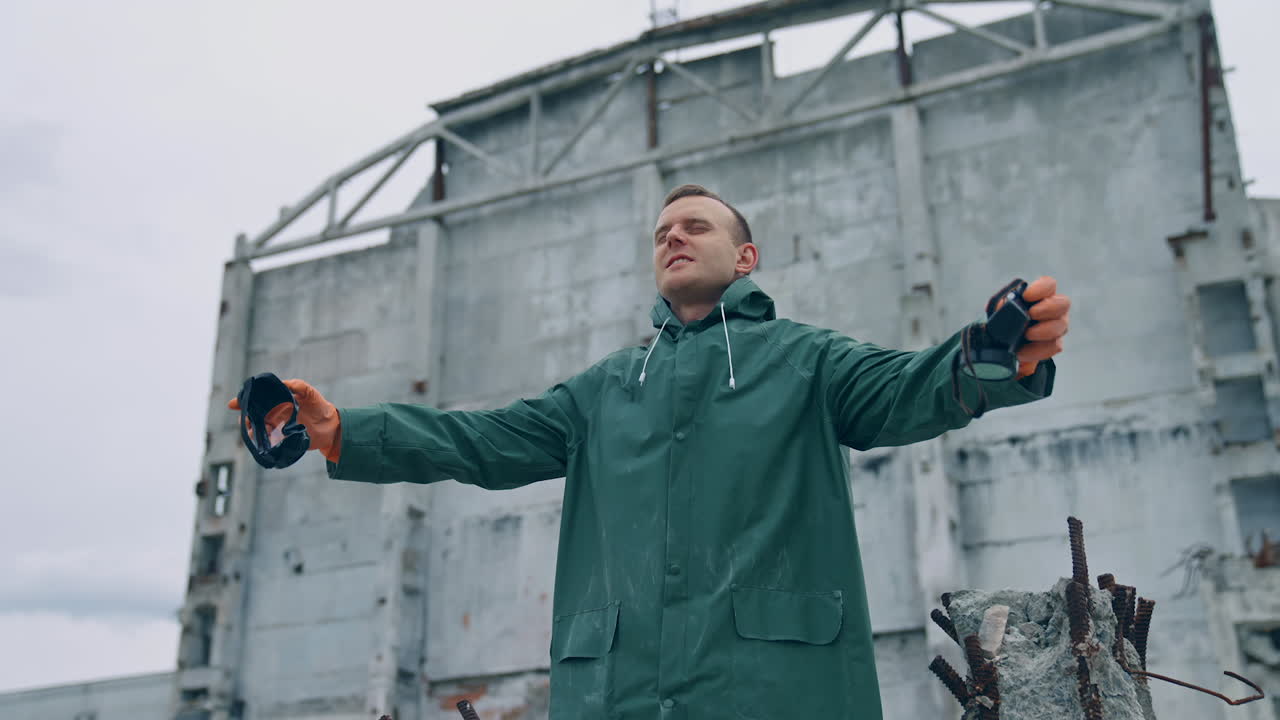 Survivor breathing deeply in destructed place. Man in protective suit holding safety gas mask in hands in enjoys fresh air on the background of ruined building.