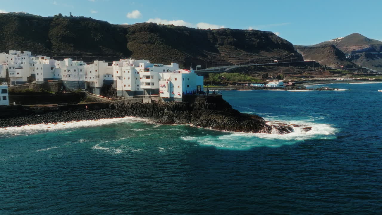 Pull out drone shot of Atlantic Ocean, shore and white neighborhood during the day in Gran Canaria, Spain