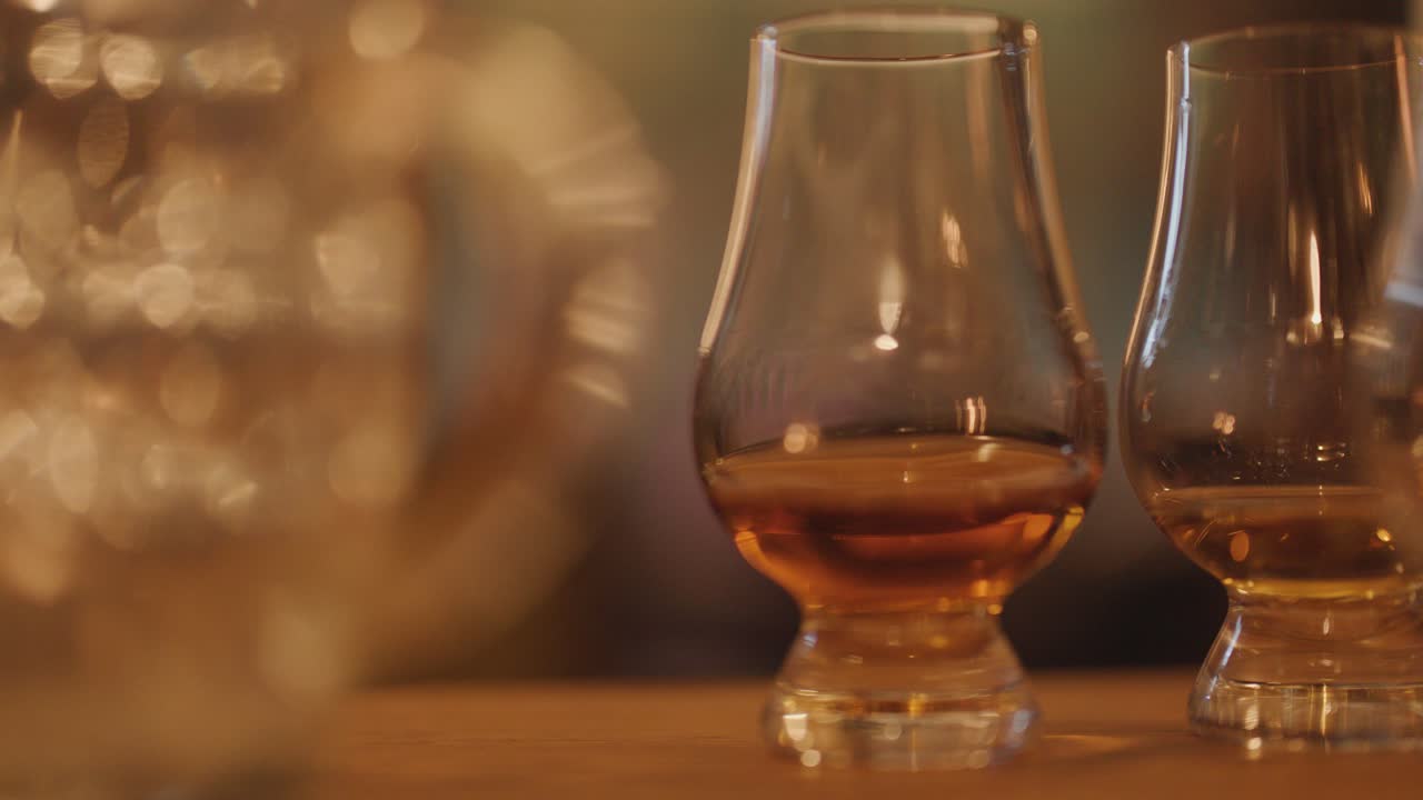 Two whisky glasses on a wooden table, warmly lit by candlelight for a cozy atmosphere