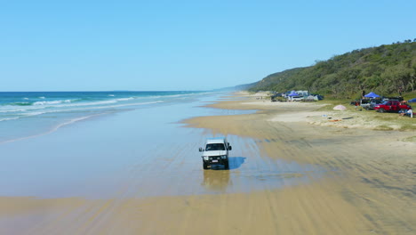 4wd-Conduciendo-En-La-Playa-De-Camping-Junto-A-Las-Olas-Azules-Del-Océano-En-Australia,-Dron-Aéreo-De-4k