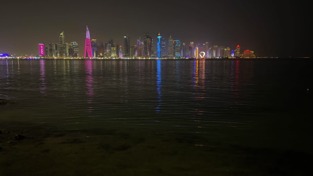 Qatar Doha Dubai City landscape at night reflection of light and tower high building skyscrapers on sea water surface small wave colorful lights in darkness dark sky modern city in middle east asia