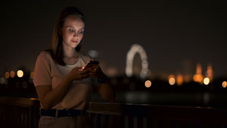 a young woman looks into the smartphone and writes text messages on the internet against the backdrop of the night city. girl businessman working on vacation remote work via mobile phone. gadget addiction