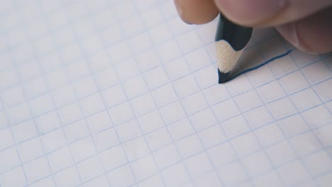 person draws line with blue pencil on checkered paper sheet