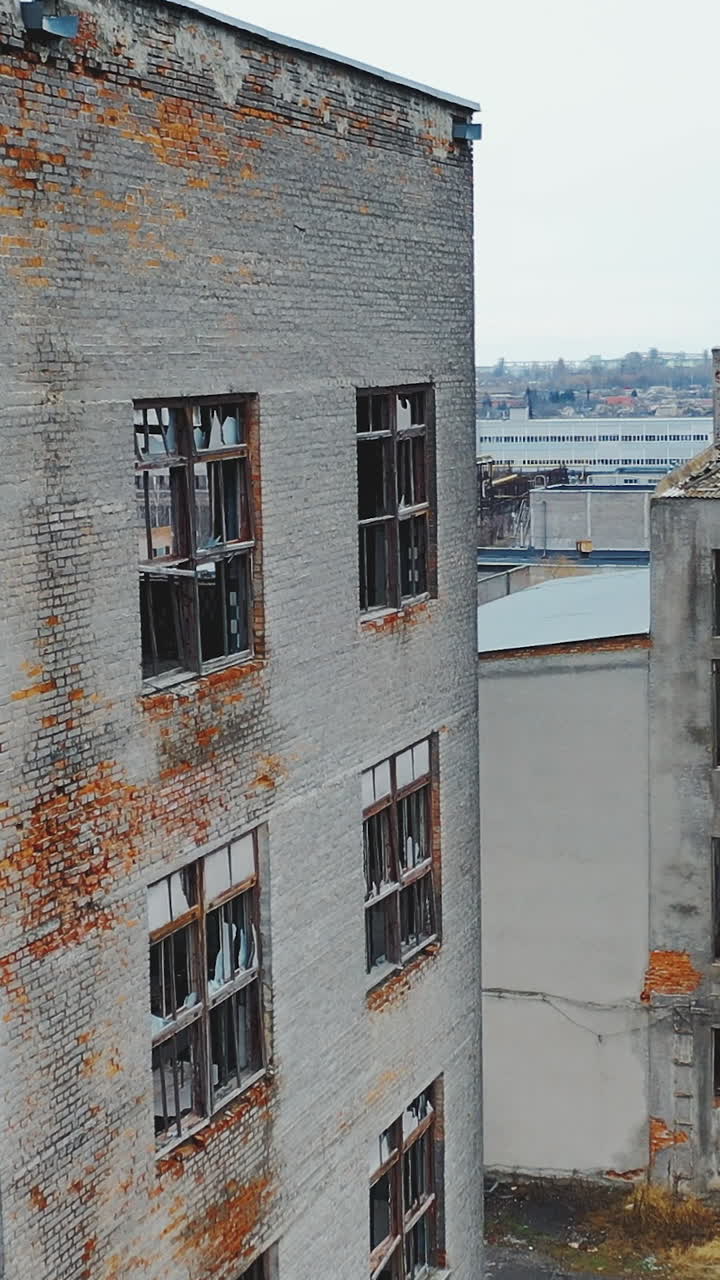 A large crumbling brick wall with broken windows. Industrial park. Aerial view. Vertical video