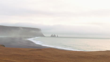 small waves crashing to shore below mountains on a hazy day in iceland