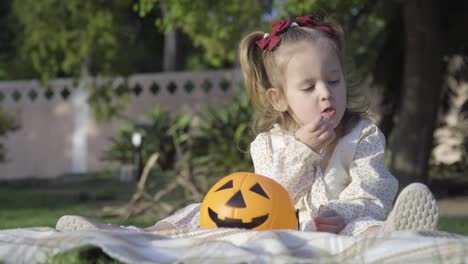 Cerca-De-Una-Adorable-Niña-Comiendo-Dulces-De-Calabaza-De-Halloween-En-El-Parque-De-La-Ciudad