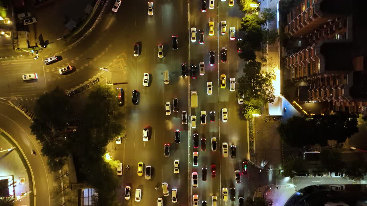 Aerial shot of rush hour traffic in Guangzhou, China, at night. Cars and taxis move through the bustling city streets, illuminated by streetlights and surrounding buildings.