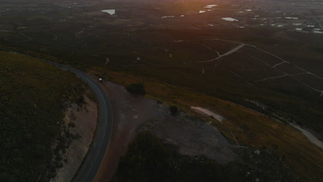 High-angle-view-of-turn-on-mountain-road-with-resting-place-and-lookout.-Tilt-up-reveal-of-wide-valley-and-romantic-sunset.-South-Africa