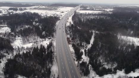 aerial revolving view of 4-lane highway cutting through snowy rural landscape with frozen river forests and farmland, seaton trail pickering ontario