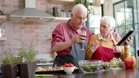 Pareja-Caucásica-Mayor-Cocinando-La-Cena-Usando-Una-Tableta-En-La-Cocina-De-Casa,-Cámara-Lenta