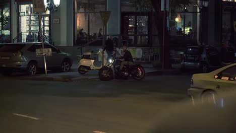 attractive rider man starting from parking place on motorbike, turns on and riding by night city street