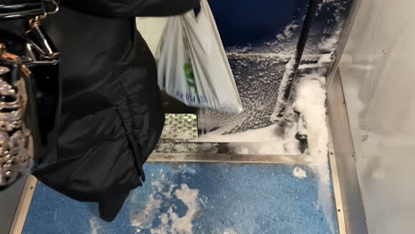 woman holds plastic bag of groceries as she disembarks from icy train with lots of snow