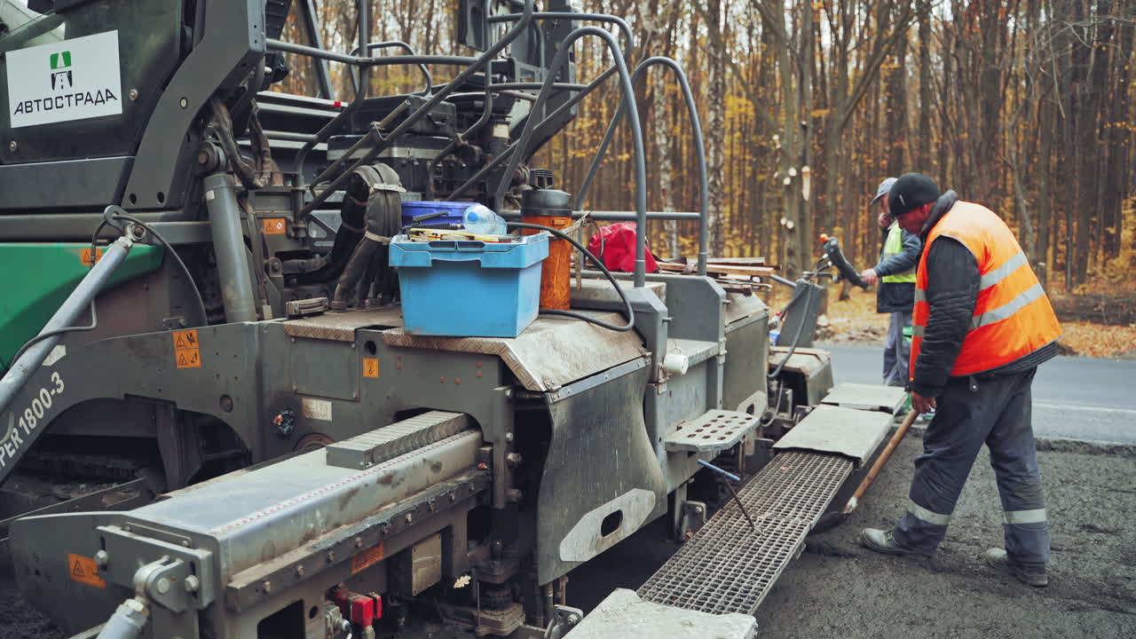 Heavy paver machine and workers put the hot asphalt on a street. Road construction workers with shovels in protective uniforms.