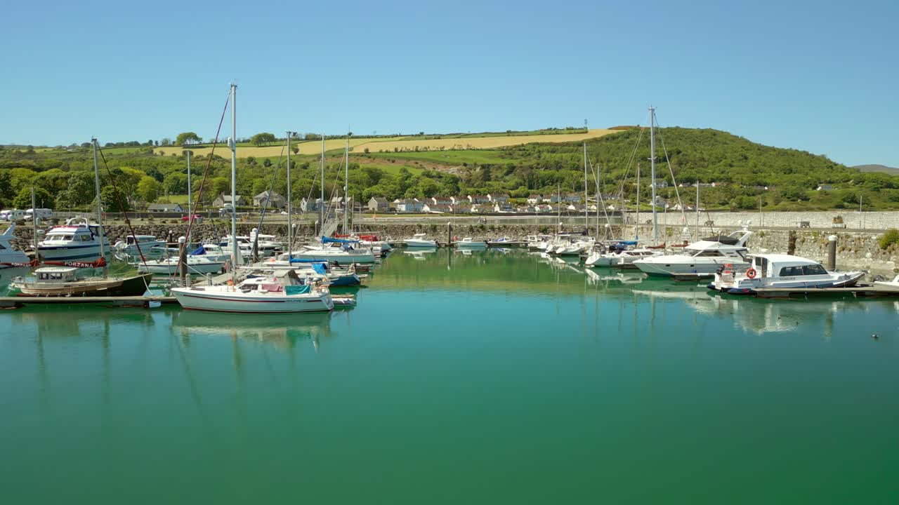 Low, reversing aerial video of the boats at Glenarm Bay, on the Causeway Coastal Route in Northern Ireland, on a bright and sunny day. Filmed in 4K, 60FPS and with Rec709 color.