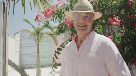 Portrait-of-happy-senior-caucasian-man-smiling-in-the-sun-by-pink-flowers,-in-slow-motion