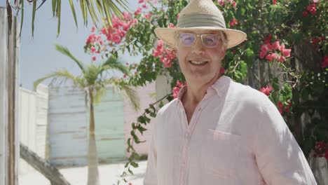 portrait of happy senior caucasian man smiling in the sun by pink flowers, in slow motion