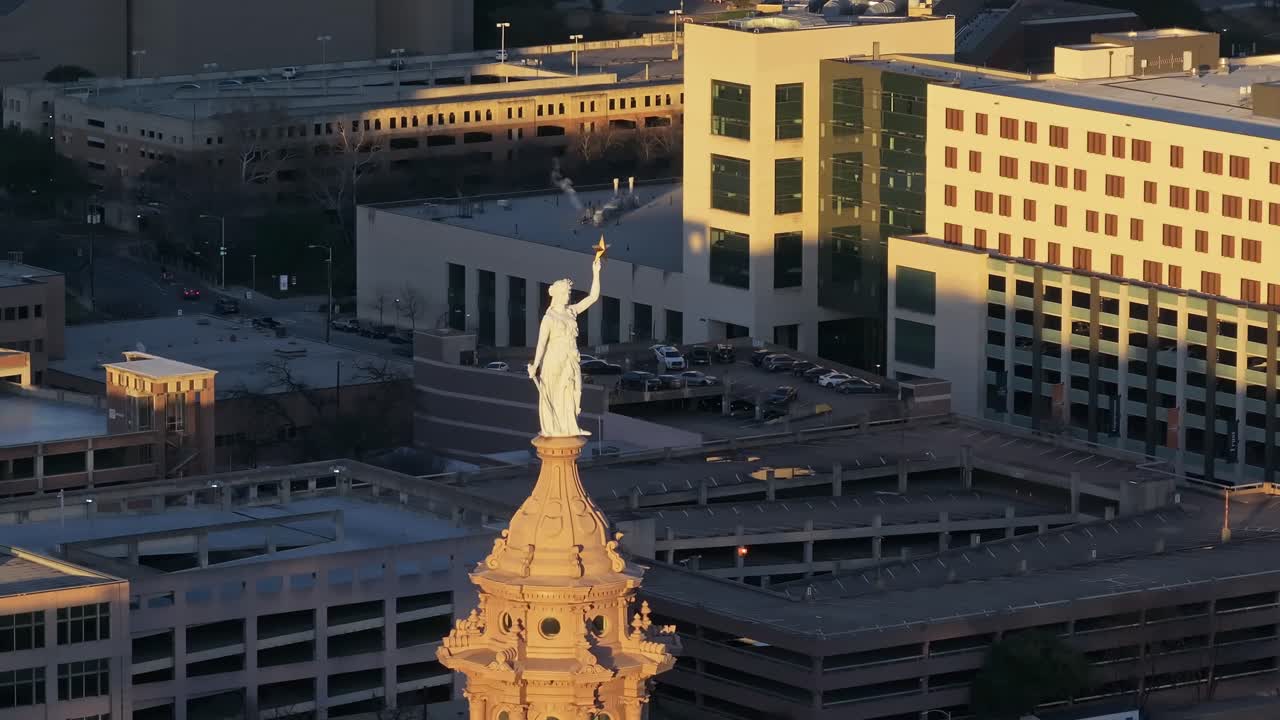 A stable drone shot focused on the Goddess of Liberty statue on top of the dome on the Texas State Capitol building in Austin Texas facing away from the sun