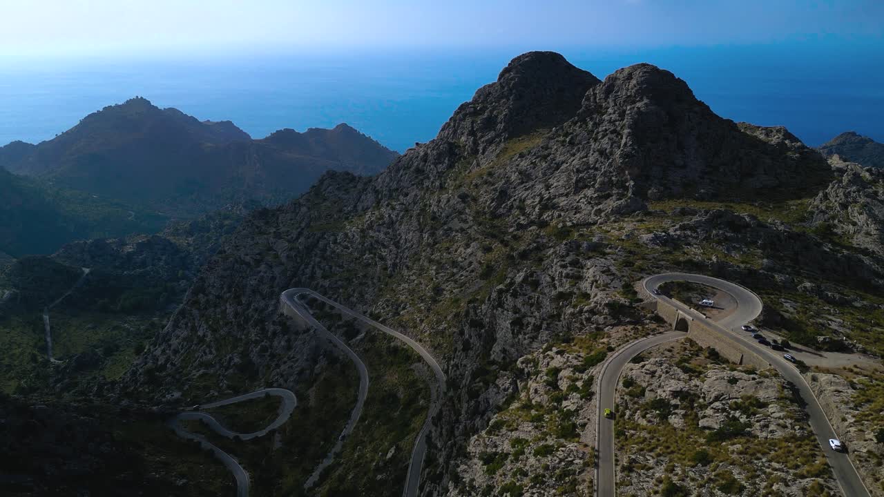 Dolly aereo medio della strada di Sa Calobra che attraversa un paesaggio montuoso sotto un cielo limpido, auto che percorrono tornanti, Maiorca - Spagna