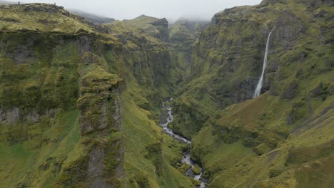 Drohnenaufnahmen-Aus-Der-Luft-Hoch-über-Bergigen-Klippen-Mit-Einem-Wasserfall-Und-Einem-Flusssystem-Darunter