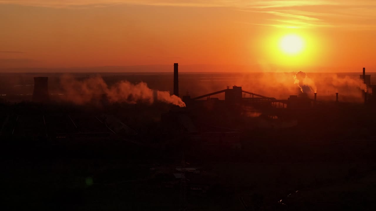 오렌지색 빛의 생생한 색조에 대비하여 연기가 방출되는 산업 굴의 실루, 높은 대조