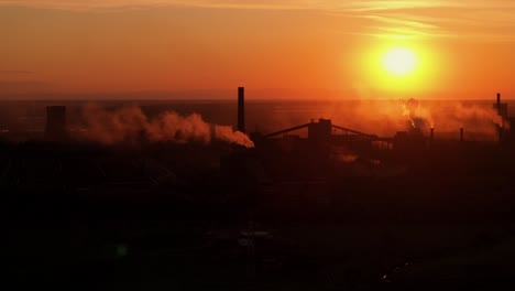 Silhouettes-of-industrial-smokestacks-with-smoke-emissions,-against-the-vivid-hues-of-orange-sunlight,-high-contrast