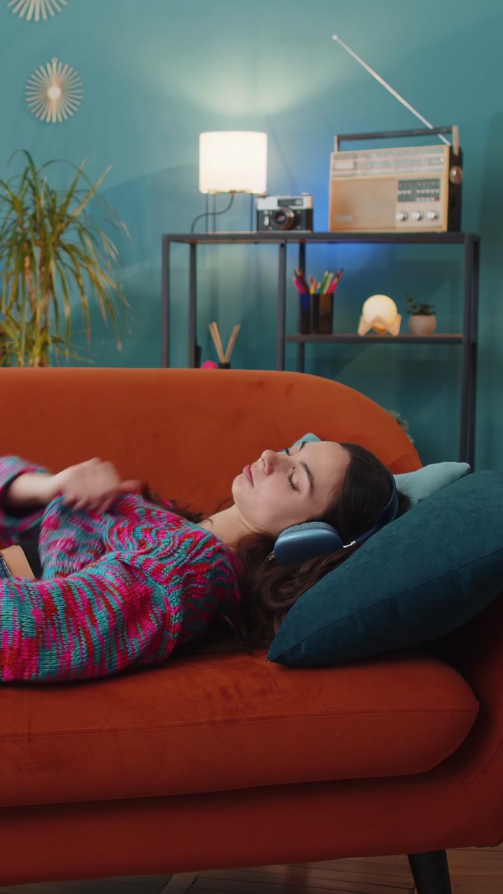 Donna felice con cuffie wireless che si rilassa e si riposa sdraiata sul divano di casa, ascoltando la sua musica preferita.