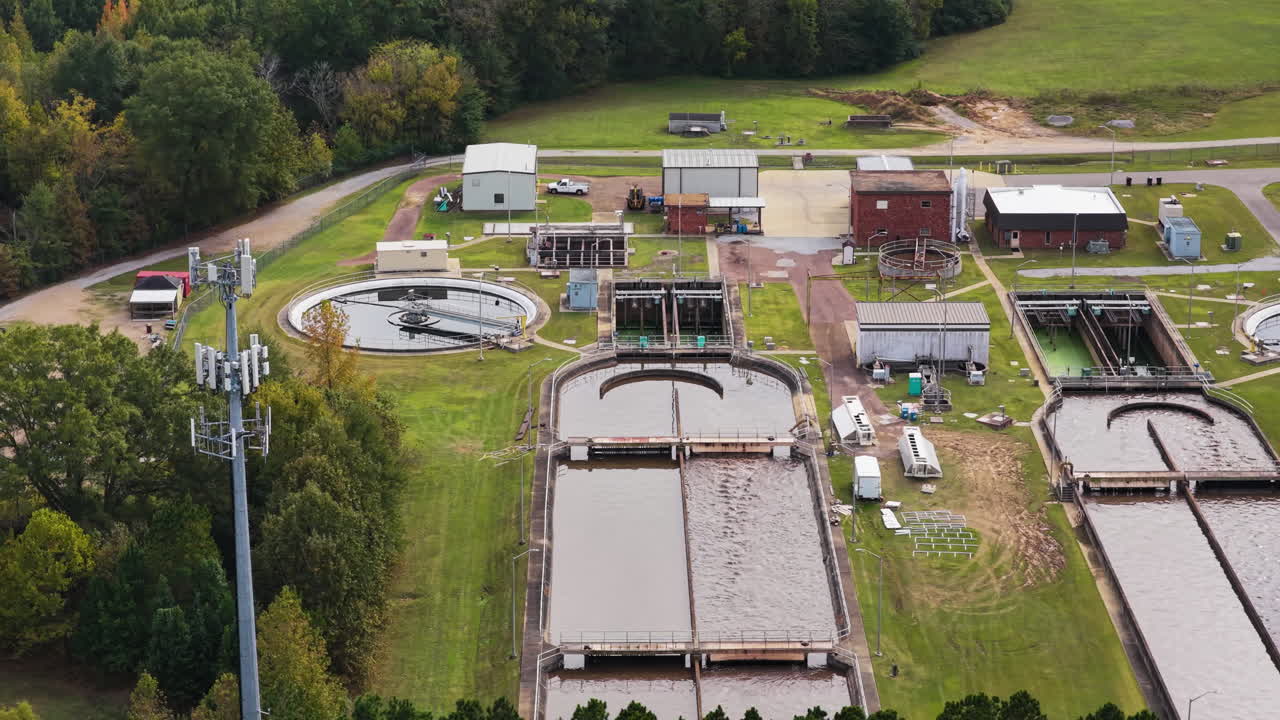 Wastewater treatment plant surrounded by trees and suburban homes, filtration circulating pools and equipment, aerial pullback