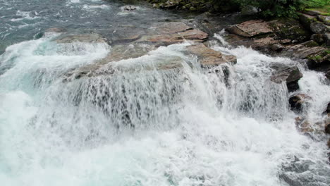 Nach-Unten-Geneigte-Kranaufnahme-Von-Kristallklarem-Gletscherschmelzwasser,-Das-über-Große-Felsen-An-Der-Spitze-Eines-Mächtigen-Wasserfalls-In-Norwegen-Stürzt