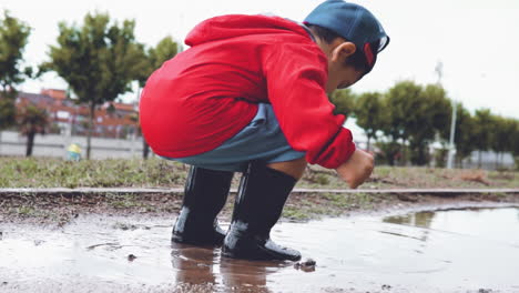 kid wearing rubber boots jumping in a puddle in slow motion